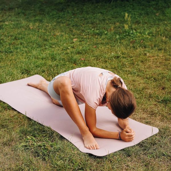 Person stretching gently on a yoga mat outdoors with a serene background.